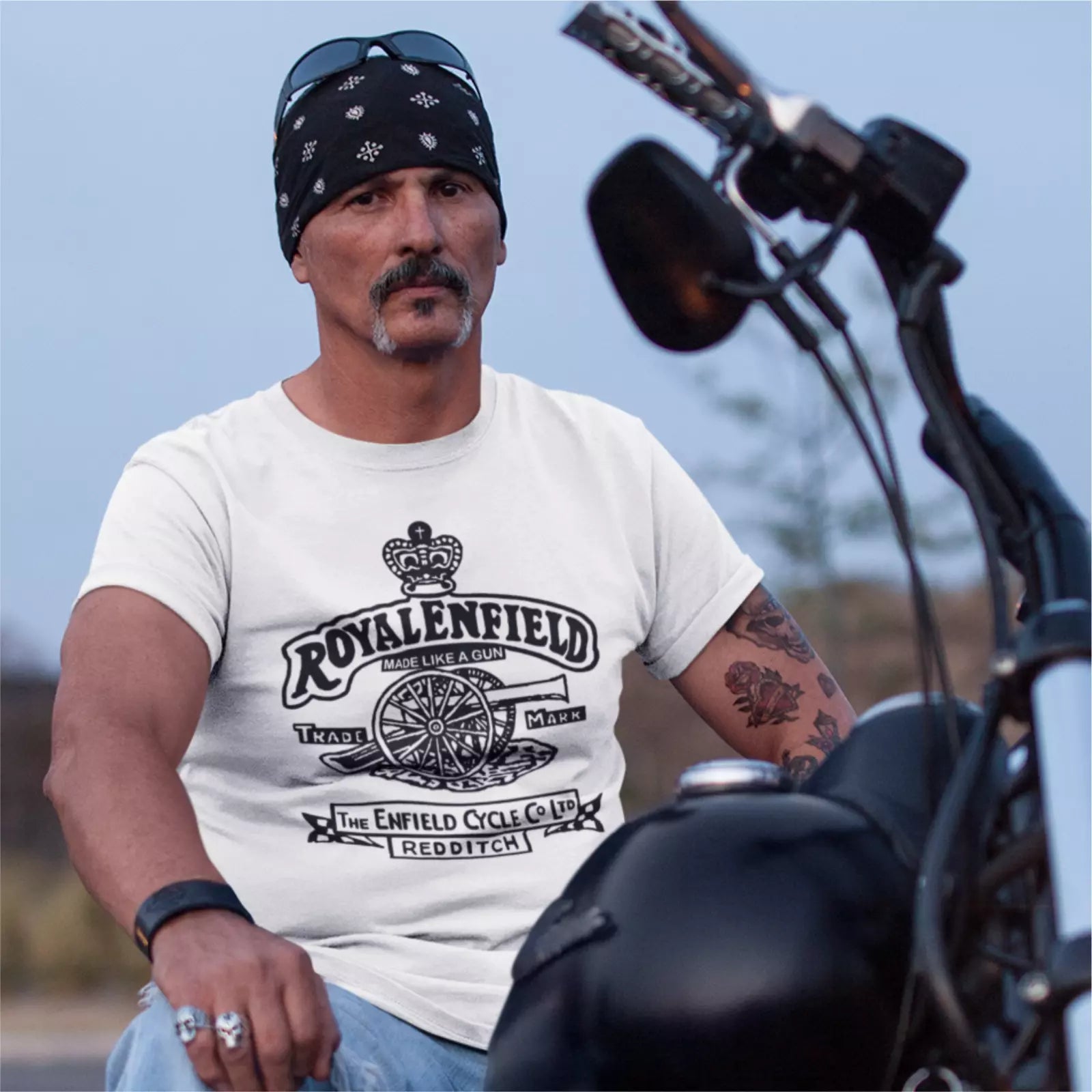 Man wearing a white t-shirt with 'Royal Enfield' branding, sitting on a motorcycle.