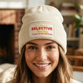 An almond ribbed knit beanie hat with a folded cuff, featuring a rectangular printed patch on the front with the text 'I Have SELECTIVE Hearing I'm Sorry You Were Not Selected' in red and yellow lettering.