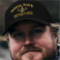 A close-up of a man wearing a black baseball cap with gold printed text reading 'ROYAL NAVY' and 'BRITAIN'S NAVY' with an anchor emblem.