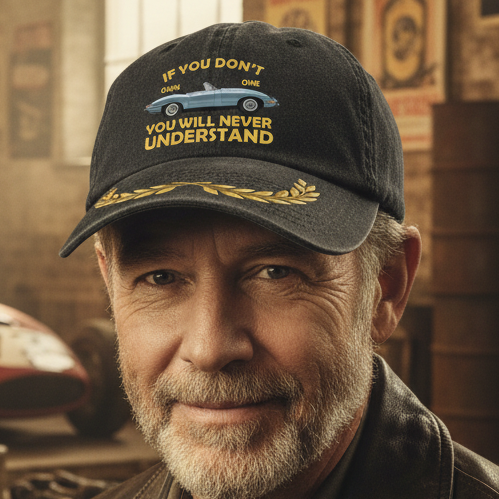 A dark gray washed baseball cap featuring a gold laurel wreath on the brim and a front graphic with a light blue convertible car and the text 'IF YOU DON'T OWN ONE YOU WILL NEVER UNDERSTAND' in gold.