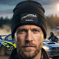A black ribbed knit beanie hat featuring a rectangular black patch on the front cuff with a white car silhouette and the word 'SUBARU' in white.