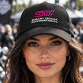 A black baseball cap featuring a pink and white printed logo and text on the front that reads 'STI' and 'SUBARU TECNICA INTERNATIONAL'.