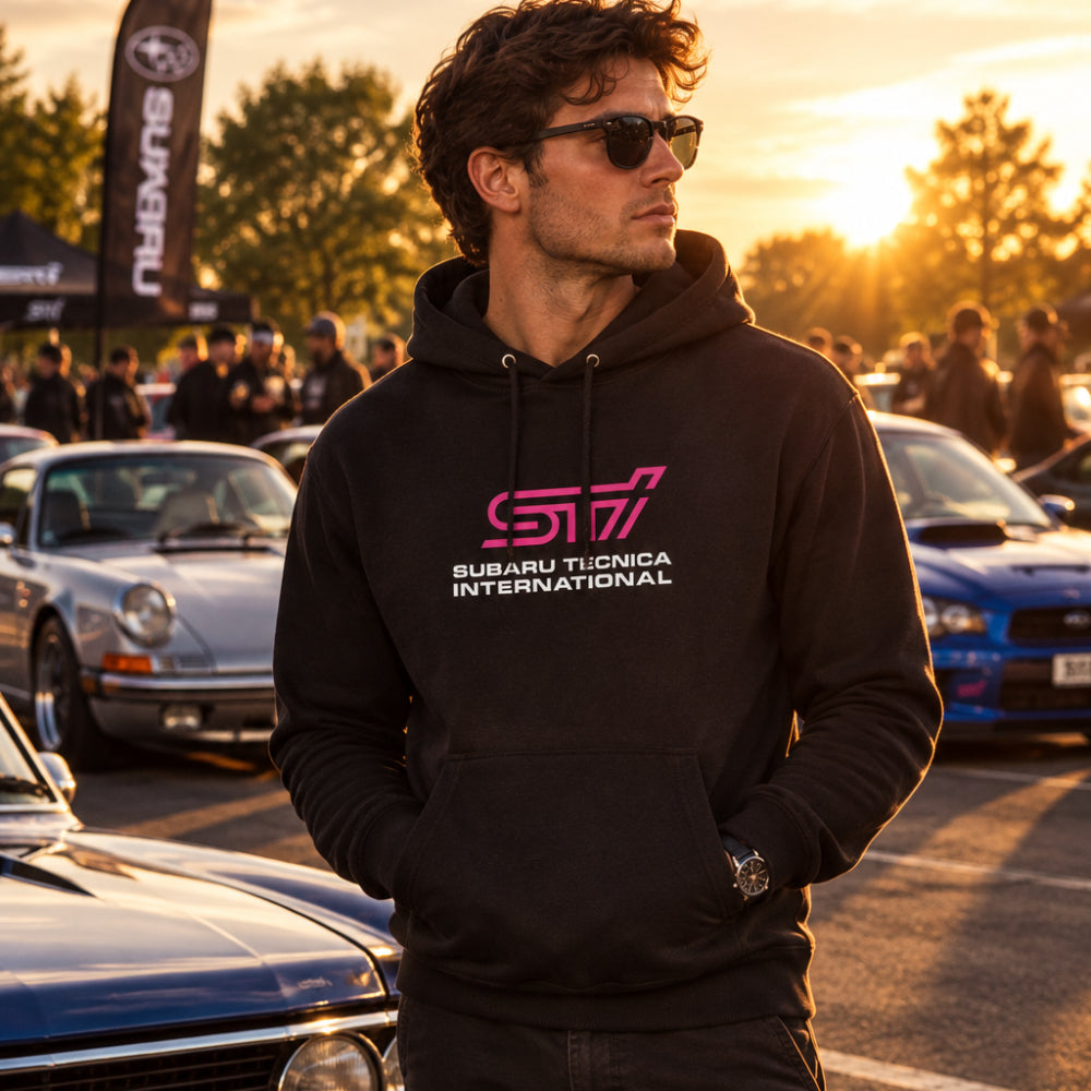 A black pullover hoodie with a pink and white SUBARU TECNICA INTERNATIONAL logo printed on the chest, displayed on a solid white background.