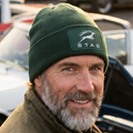 A dark forest green ribbed knit beanie hat featuring a white printed Triumph Stag logo patch on the front cuff.