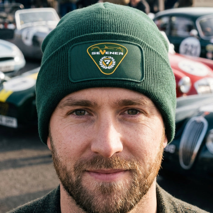 A dark green ribbed knit beanie hat featuring a rectangular patch on the front cuff with a green and gold shield emblem and the word 'SEVENER'.