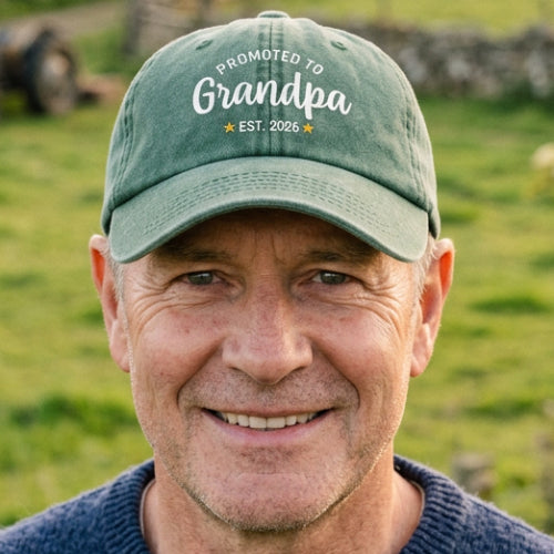 A green-washed baseball cap with white printed text reading 'PROMOTED TO Grandpa EST. 2026' on the front and 'Custom Text' on the brim, shown on a plain white background.