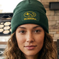 A bottle green ribbed knit beanie hat featuring a rectangular patch on the front cuff with the yellow Subaru logo and brand name.