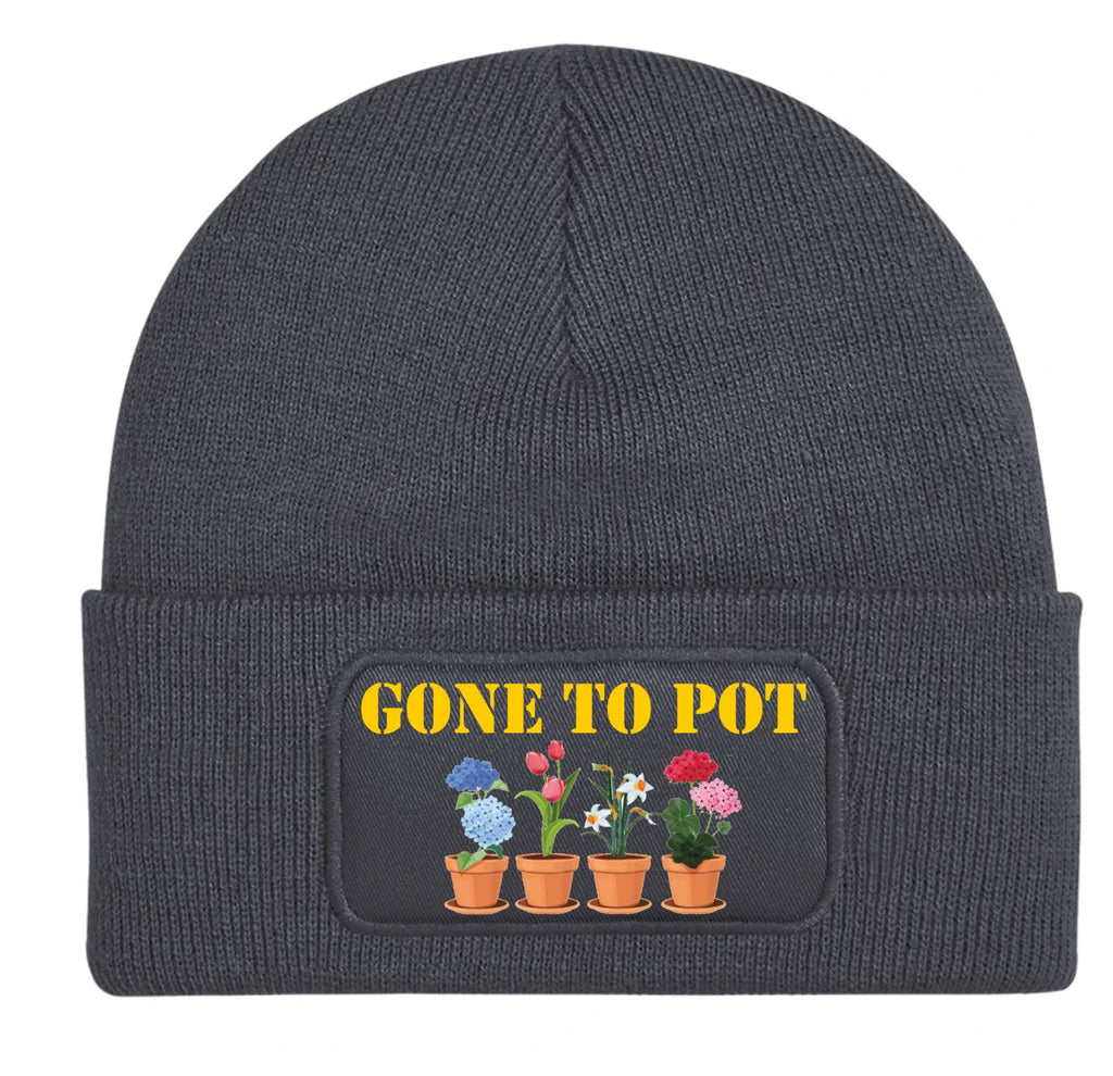 A dark gray ribbed knit beanie hat with a folded cuff, featuring a rectangular patch on the front that reads 'GONE TO POT' in yellow text above four colorful potted flowers.