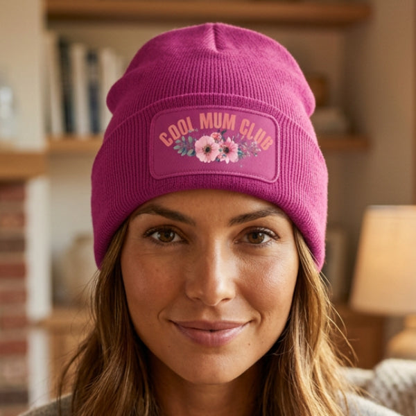 A Fuchsia ribbed knit beanie with a folded cuff, featuring a rectangular embroidered patch on the front that reads 'COOL MUM CLUB' in pink lettering above a pink and green floral design.
