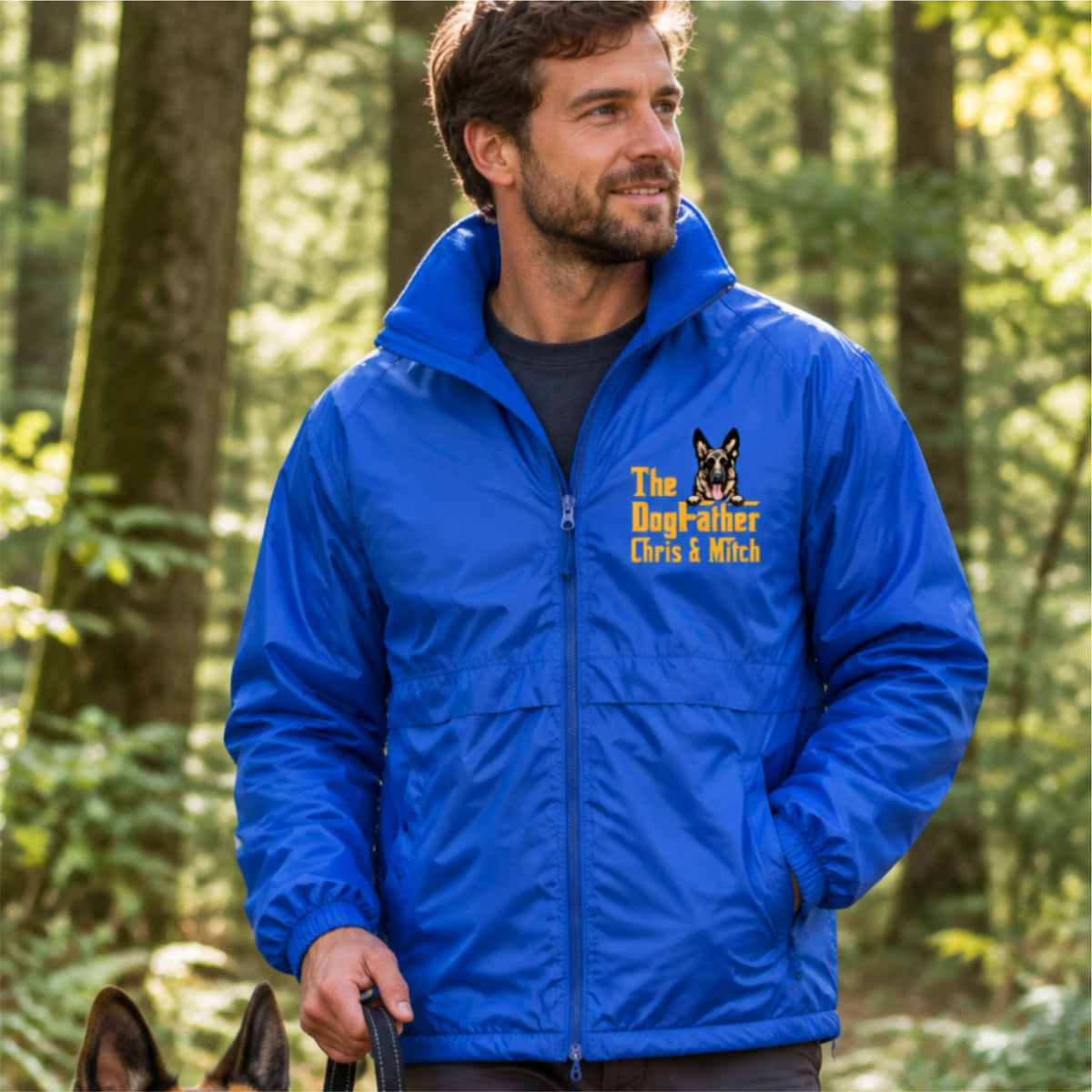 A royal blue zip-up windbreaker jacket with a stand-up collar, featuring a yellow and black graphic on the left chest that reads 'The Dog Father Chris & Mitch' alongside a dog illustration. The jacket is displayed on a clean white background.
