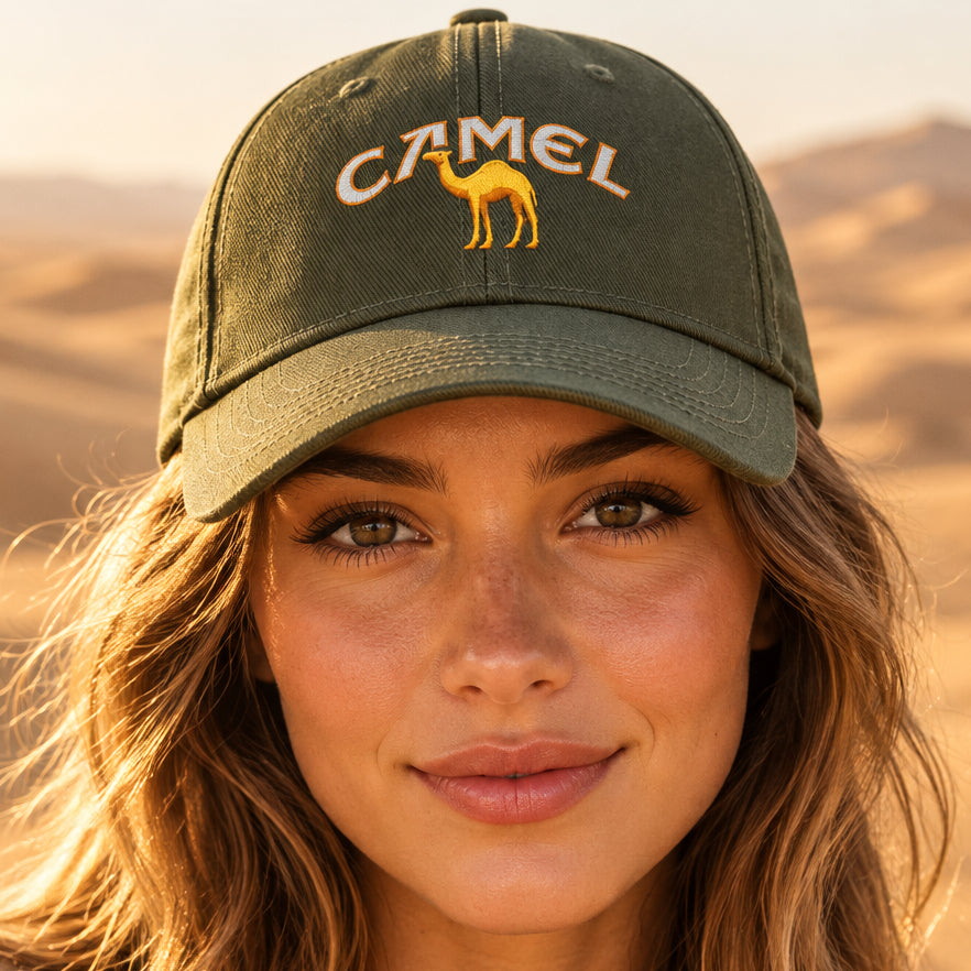 An olive green baseball cap featuring a printed design on the front with the word 'CAMEL' in white outlined letters and a yellow camel silhouette.