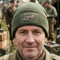 An olive green ribbed knit beanie hat with a folded cuff, featuring a rectangular printed patch on the front that reads 'WILLY'S JEEP 1911-1942' and shows a vintage jeep illustration.