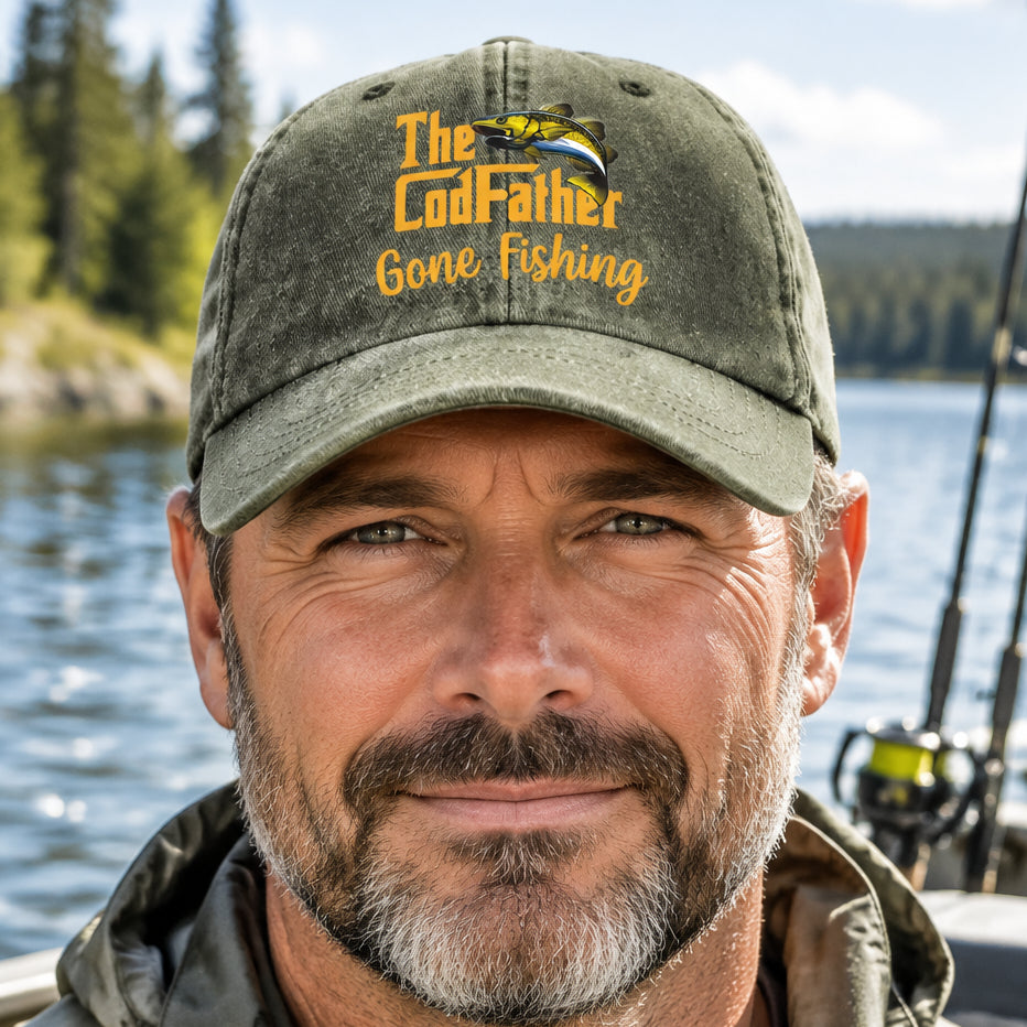 An olive-green cotton baseball cap with printed text and a fish graphic. The front features the words 'The CodFather' in orange-yellow lettering alongside an porinted yellow, black, and blue bass fish.