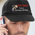 Black cap with humorous text and skeleton design worn by a person on the phone.