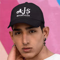 Person wearing a black cap with 'AJS Motorcycles' logo against a pink and blue background