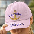 Pink cap with anchor and 'Captain Rebecca' text held by a person outdoors.