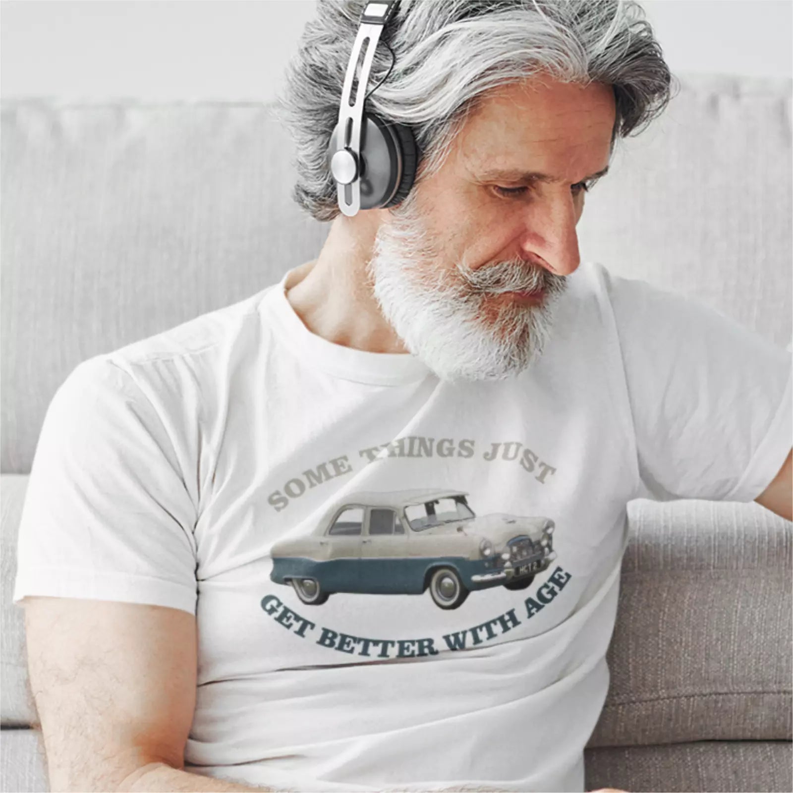 Man wearing headphones and a white t-shirt with a graphic and text, sitting on a couch.