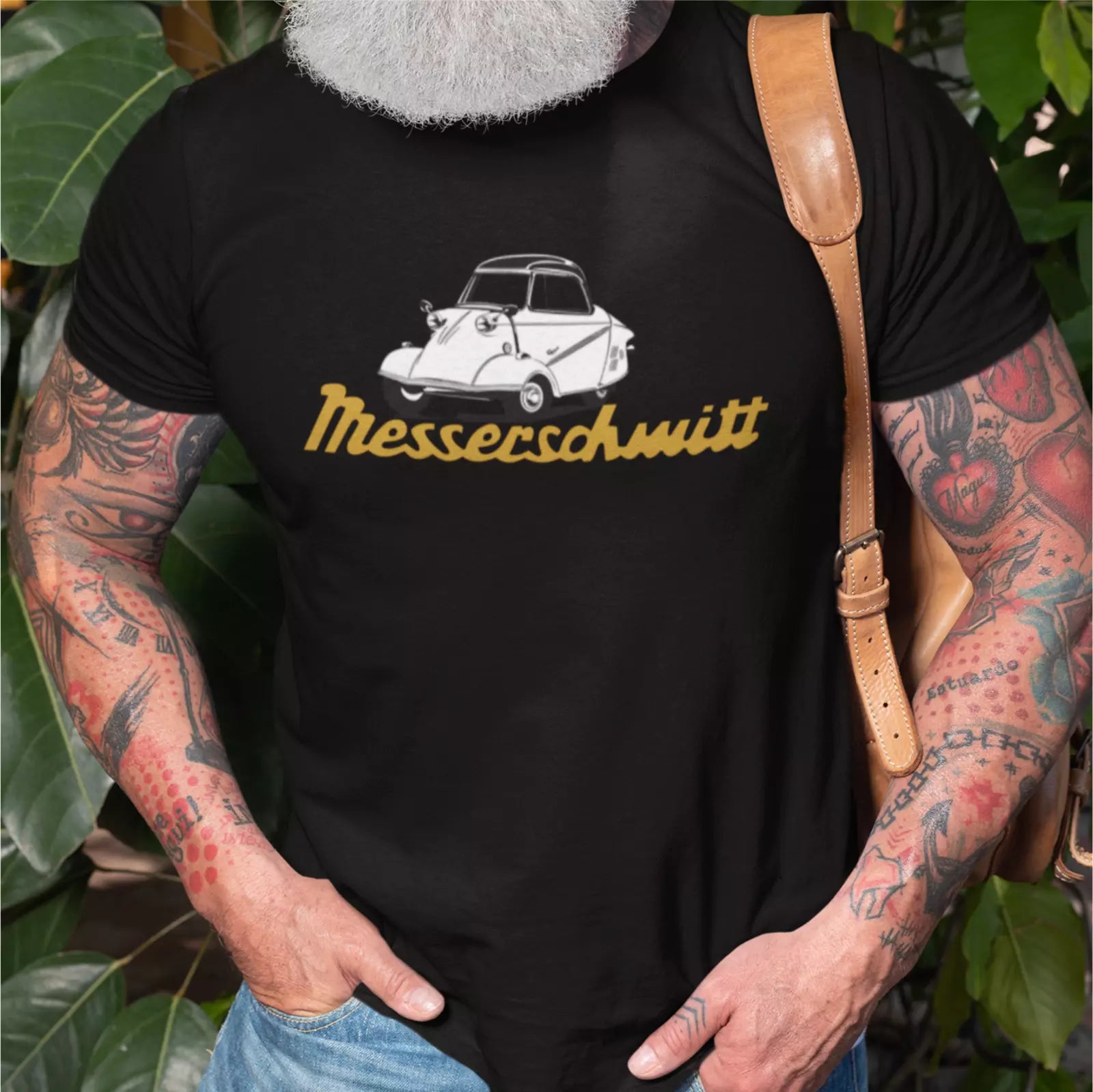 Person wearing a black t-shirt with a graphic design and text, standing among green leaves.