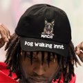 Person wearing a black cap with a dog illustration and text, against a blurred background