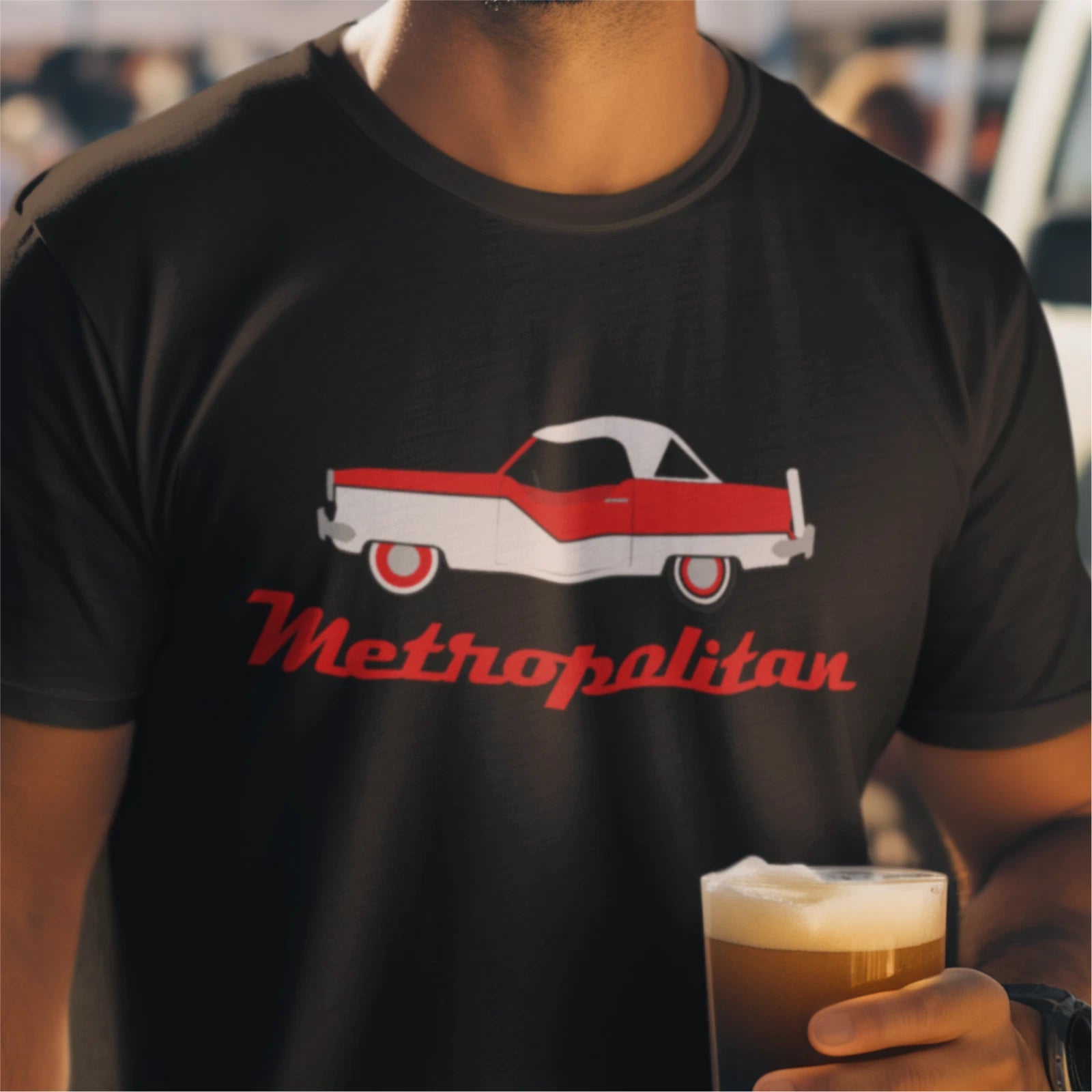 Person wearing a black t-shirt with a red and white car graphic and 'Metropolitan' text, holding a beer.