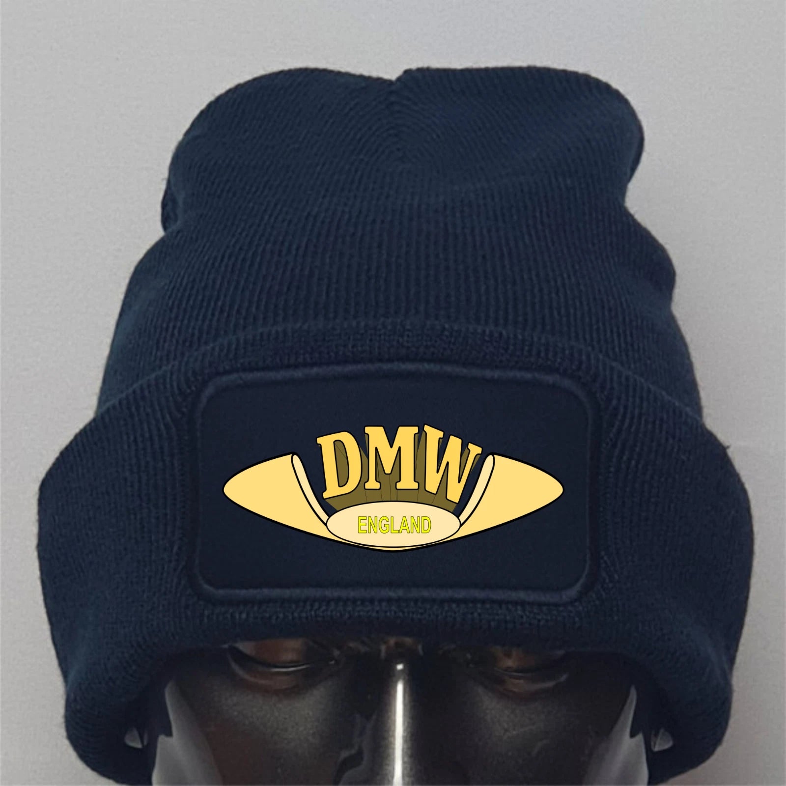 Navy blue beanie with gold 'DMW England' logo on a gray background