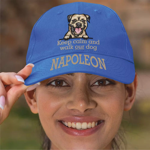 Blue cap with dog illustration and text held by a person, against a blurred natural background