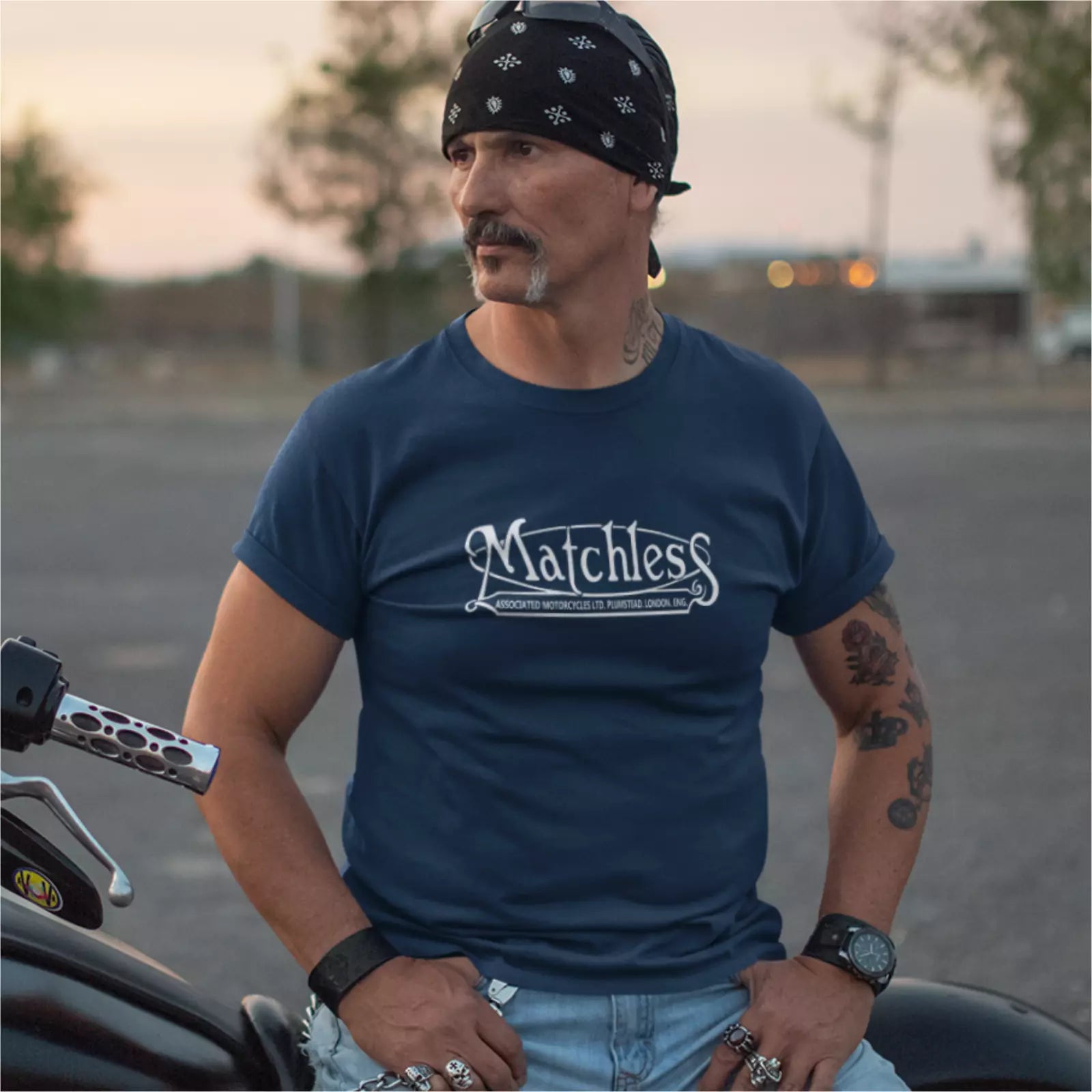 Man wearing a navy blue 'Matchless' t-shirt standing next to a motorcycle.