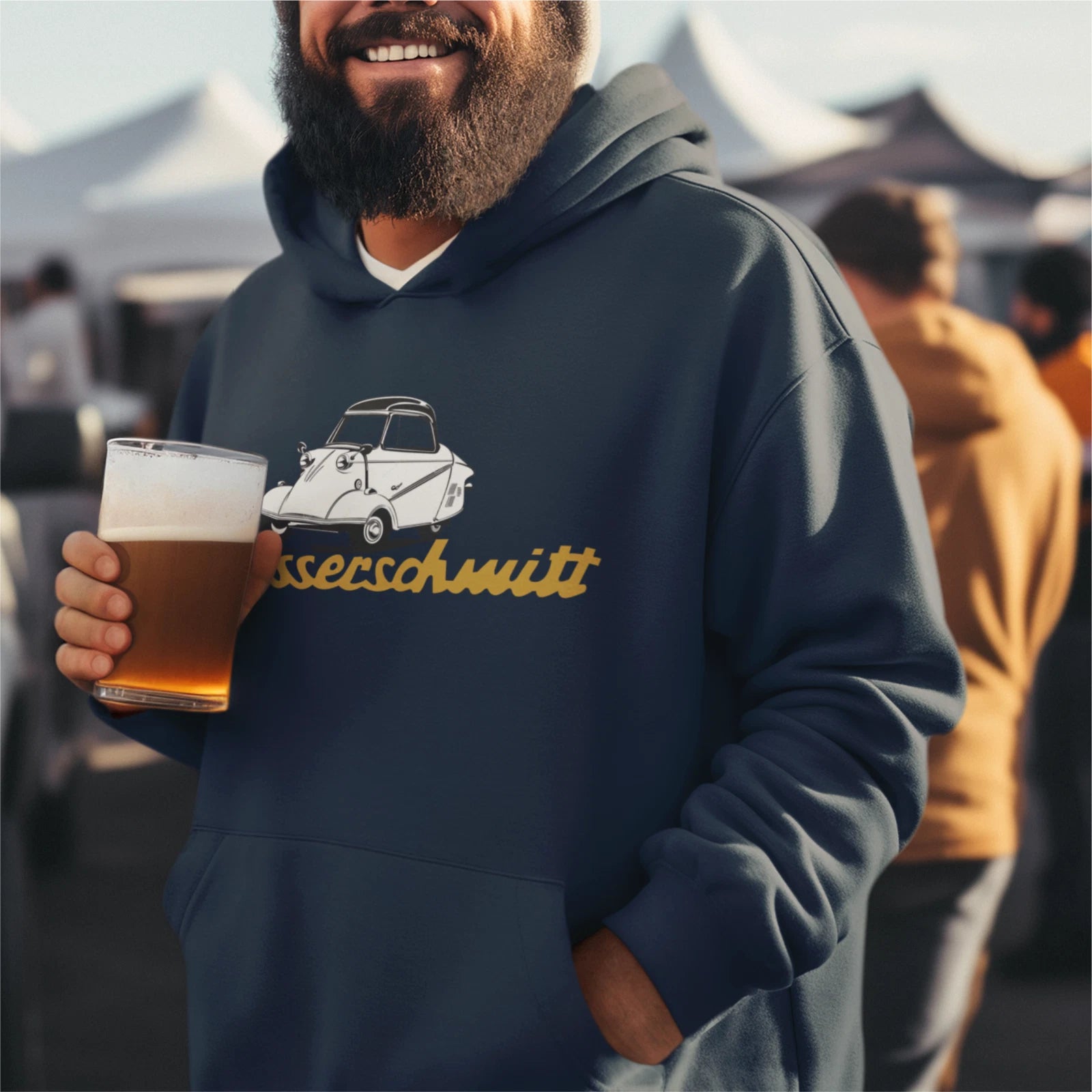 Man wearing a hoodie with a car design and text, holding a beer at an outdoor event.